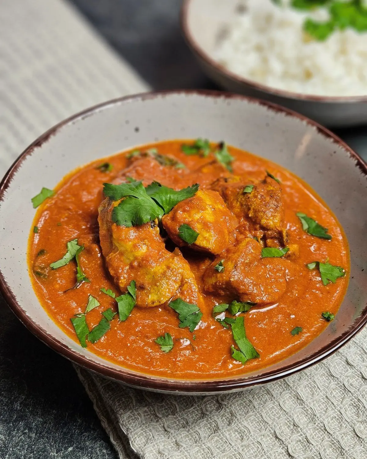 Chicken Tikka Masala in einer Schüssel mit einer Schüssel Reis im Hintergrund