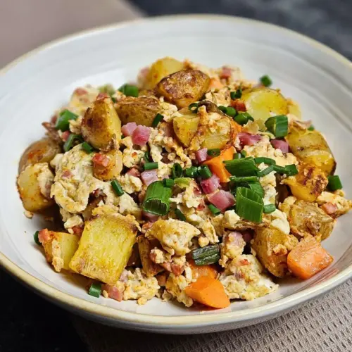 Kartoffelpfanne mit Rührei und Speck auf einem Teller angerichtet
