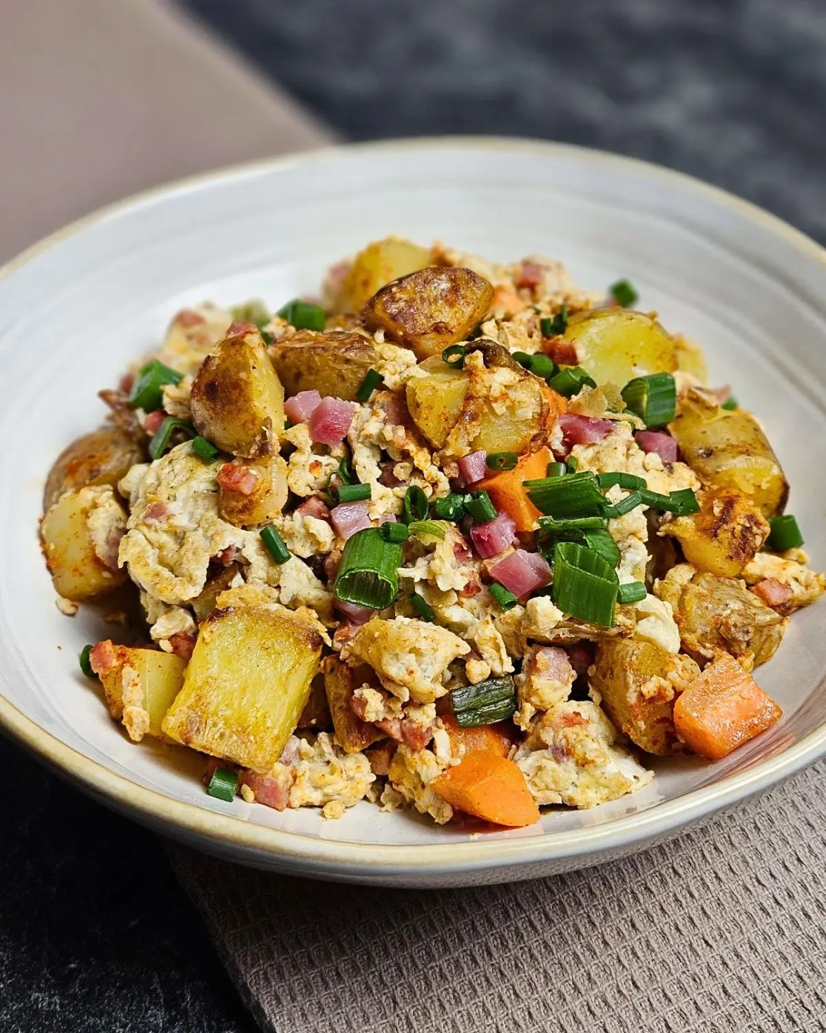 Kartoffelpfanne mit Rührei und Speck auf einem Teller angerichtet