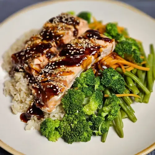 Lachs Teriyaki mit Naturreis und knackigem Gemüse auf einem Teller angerichtet und mit Sesam bestreut