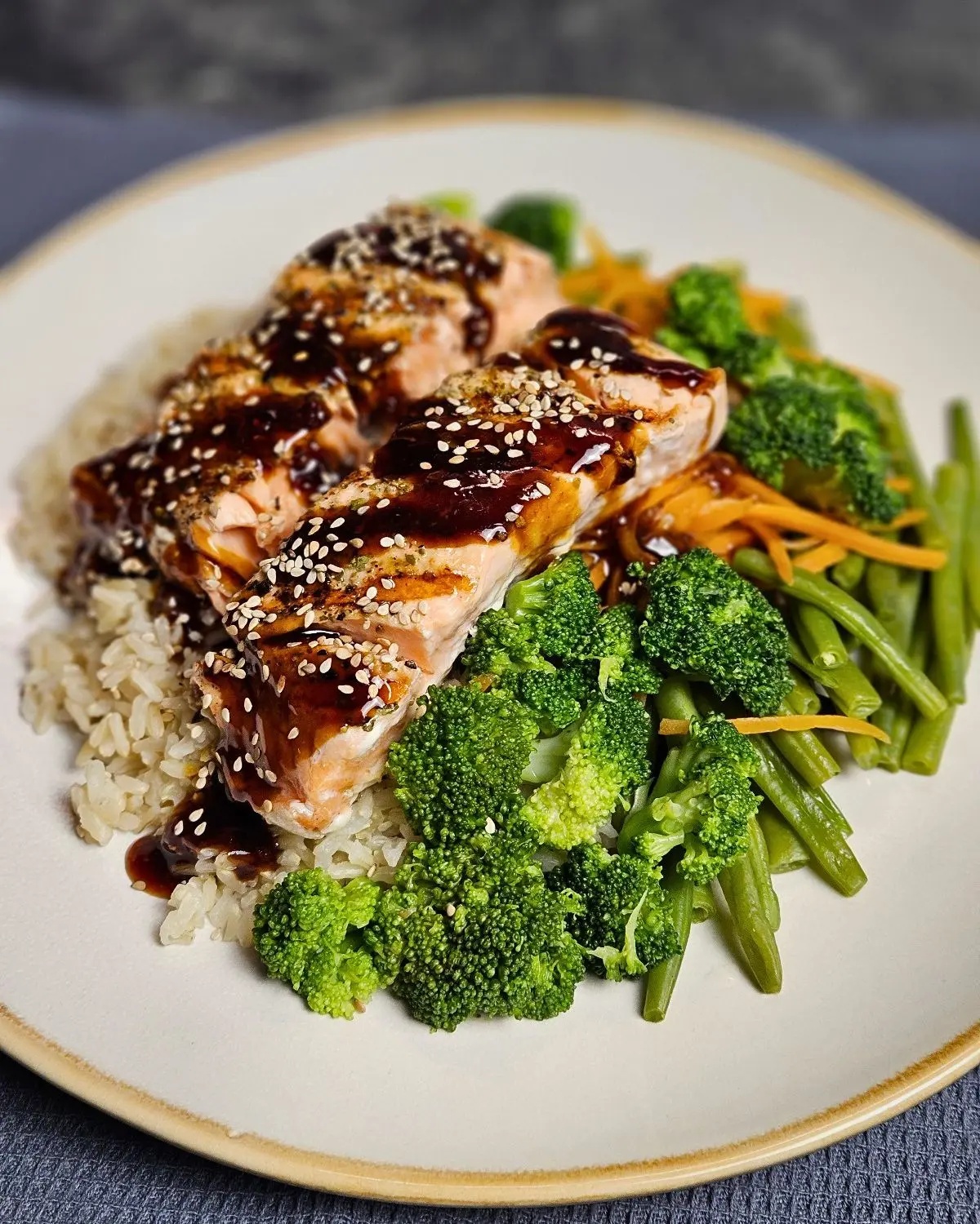 Lachs Teriyaki mit Naturreis und knackigem Gemüse auf einem Teller angerichtet und mit Sesam bestreut