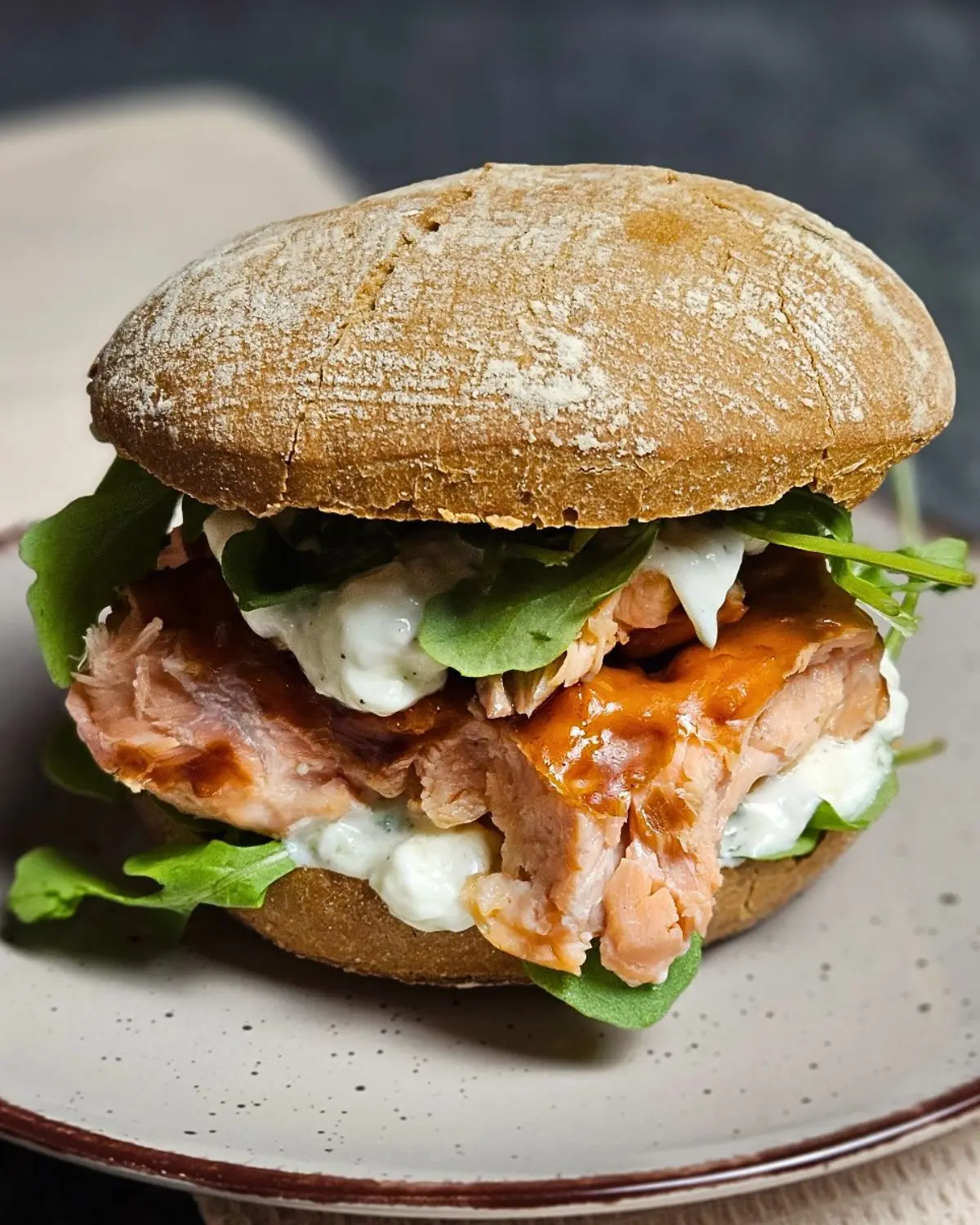 Pulled Salmon Burger mit Rucola und cremiger Gurken-Quark-Sauce auf einem Teller angerichtet