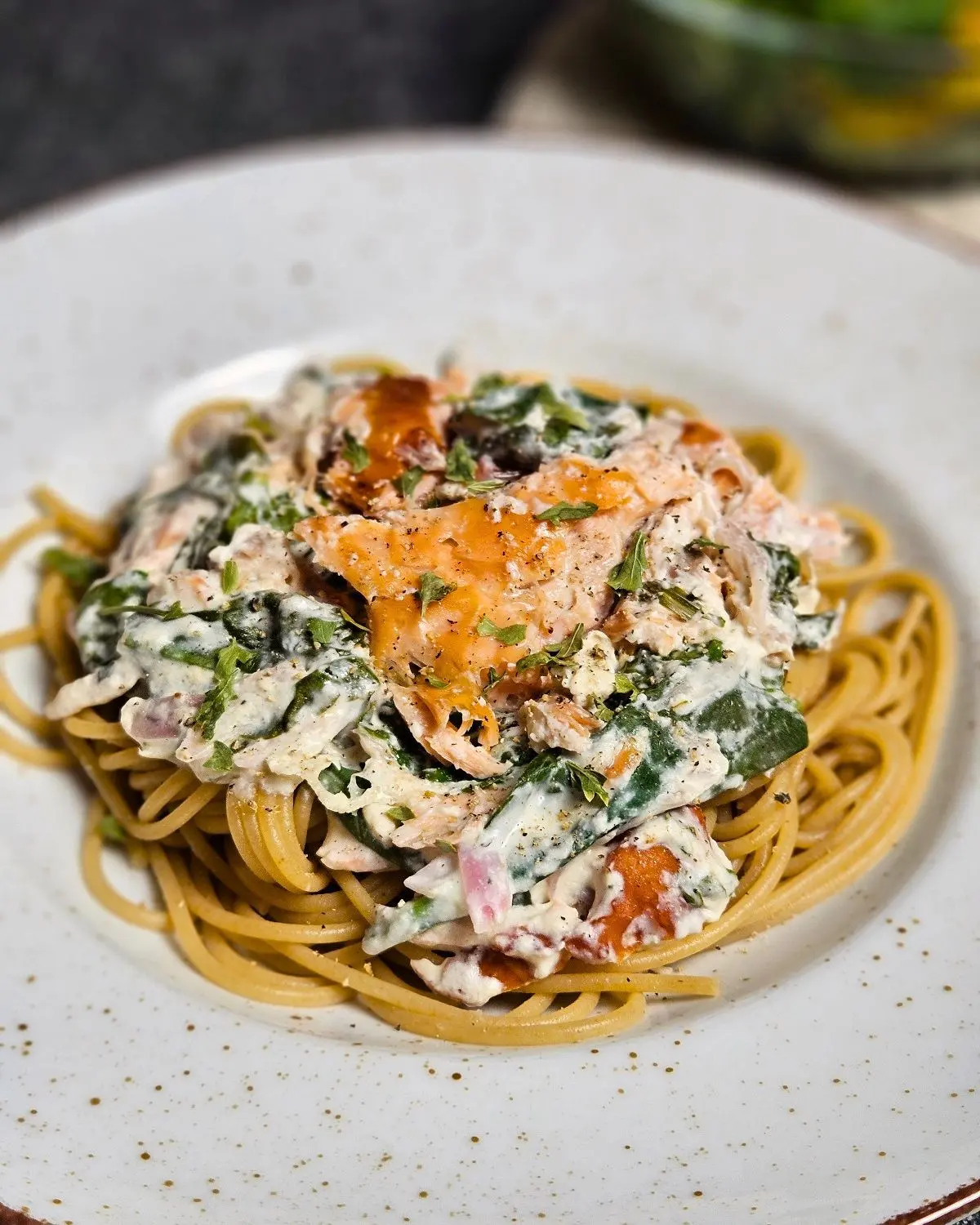 Pulled Salmon Pasta mit cremiger Frischkäse-Spinat-Sauce auf einem Teller mit einem Salat im Hintergrund