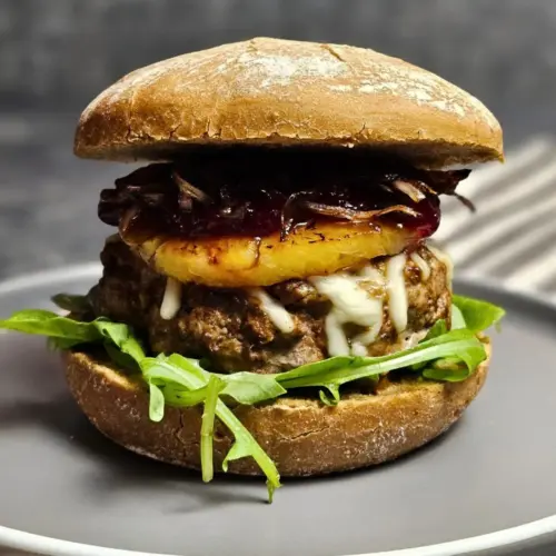 Saftiger Burger mit Rindfleisch, Ananas und Preiselbeeren auf einem Teller angerichtet