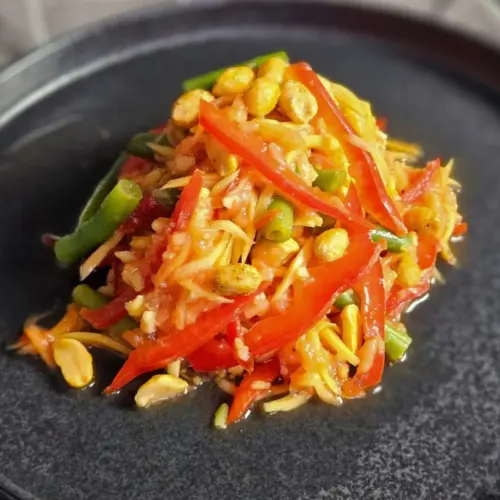 Thailändischer Papayasalat mit grünen Bohnen und Paprika auf einem Teller angerichtet