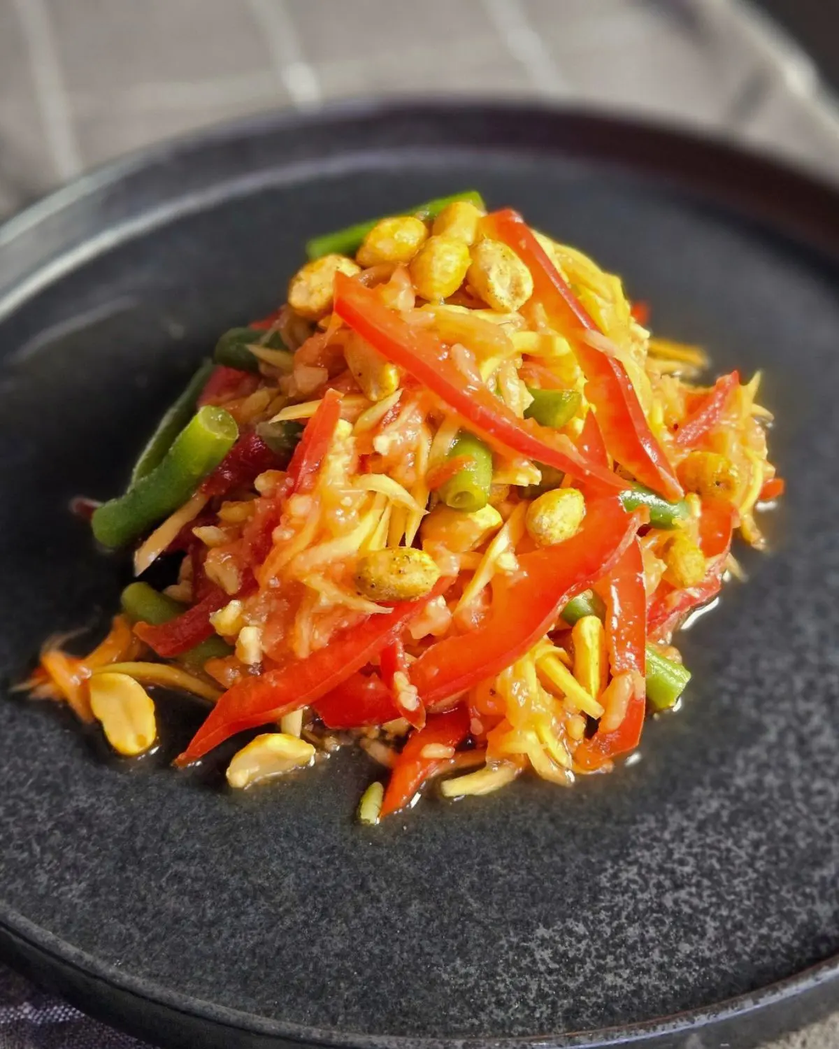 Thailändischer Papayasalat mit grünen Bohnen und Paprika auf einem Teller angerichtet
