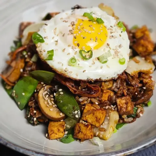 Vegetarisches Nasi Goreng mit Tofu und Ei auf einem Teller angerichtet