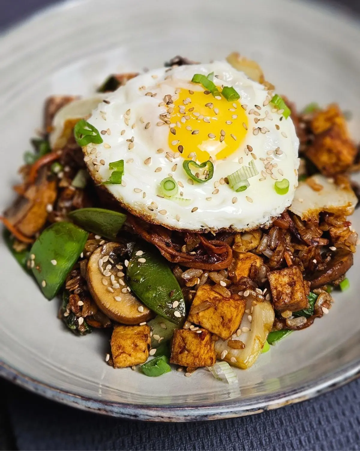 Vegetarisches Nasi Goreng mit Tofu und Ei auf einem Teller angerichtet