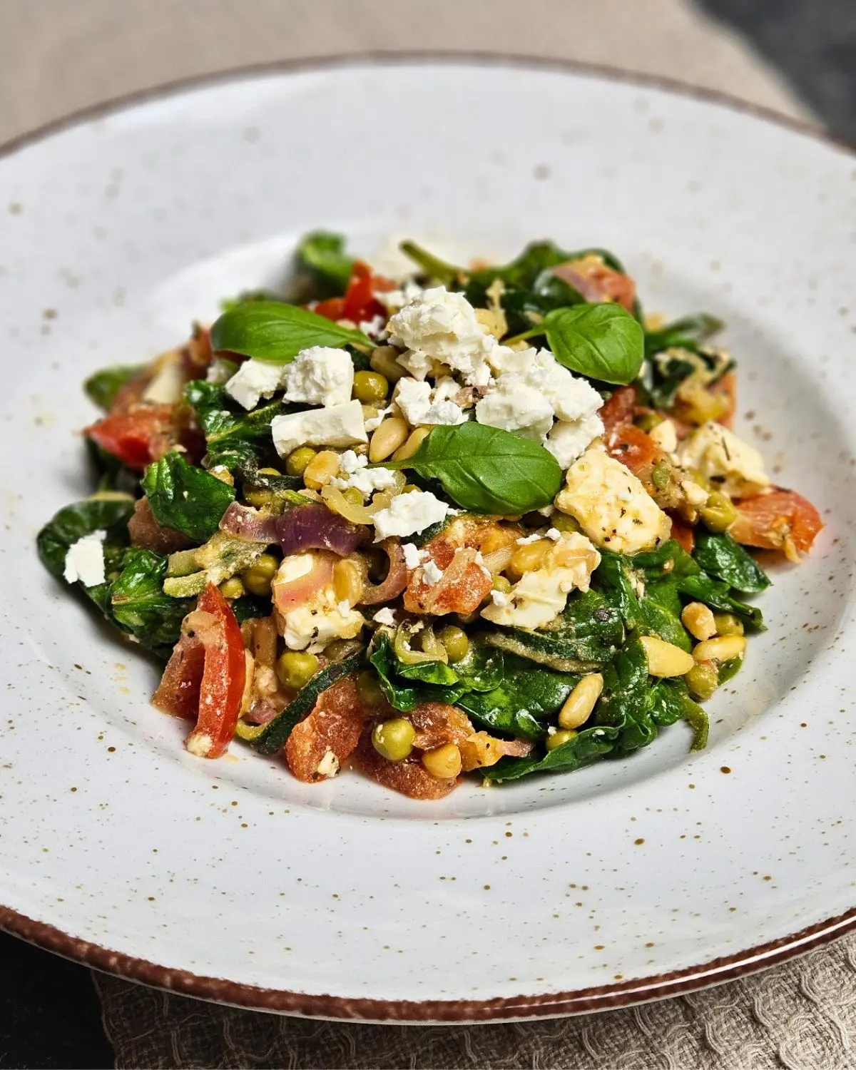 Zoodles mit Feta, Spinat und Erbsen auf einem Teller angerichtet
