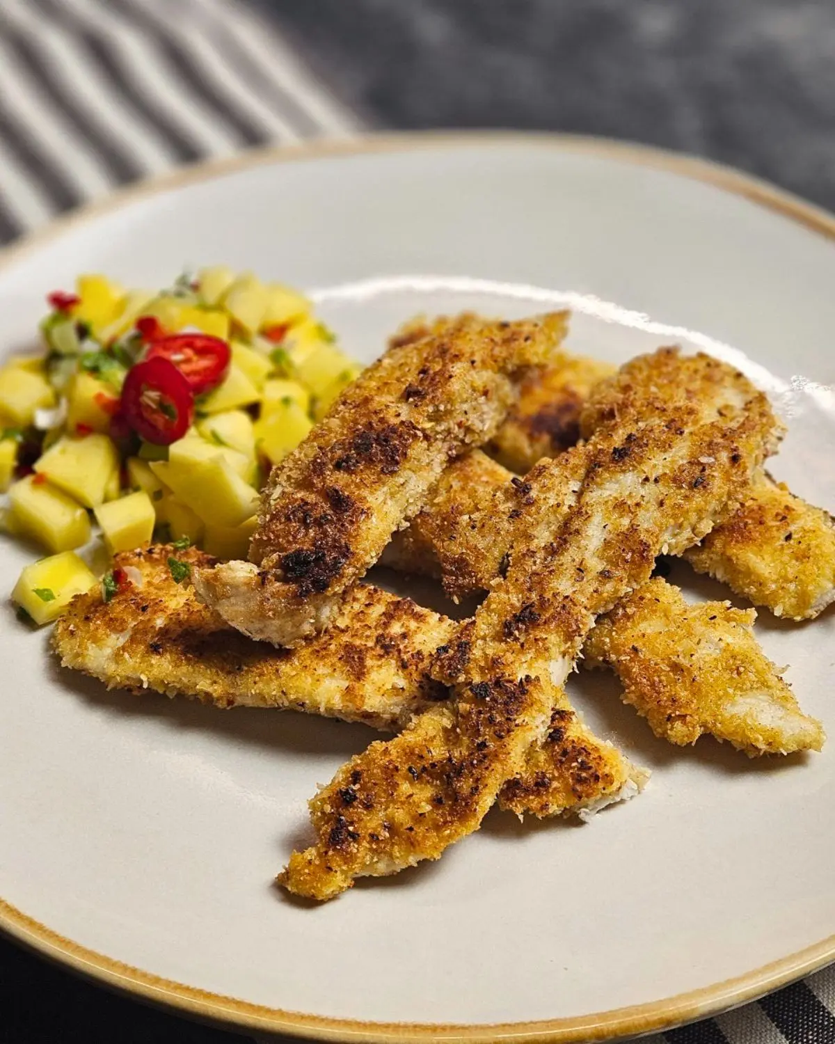 Knuspriges Kokos-Hähnchen mit frischer Mango-Salsa, saftige Hähnchenstreifen mit Mango-Salsa auf einem Teller angerichtet