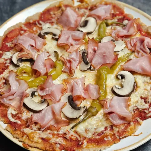 High Protein Pizza mit Skyr-Teig mit Schinken, Champignons und Pepperoni belegt und auf einem Teller serviert