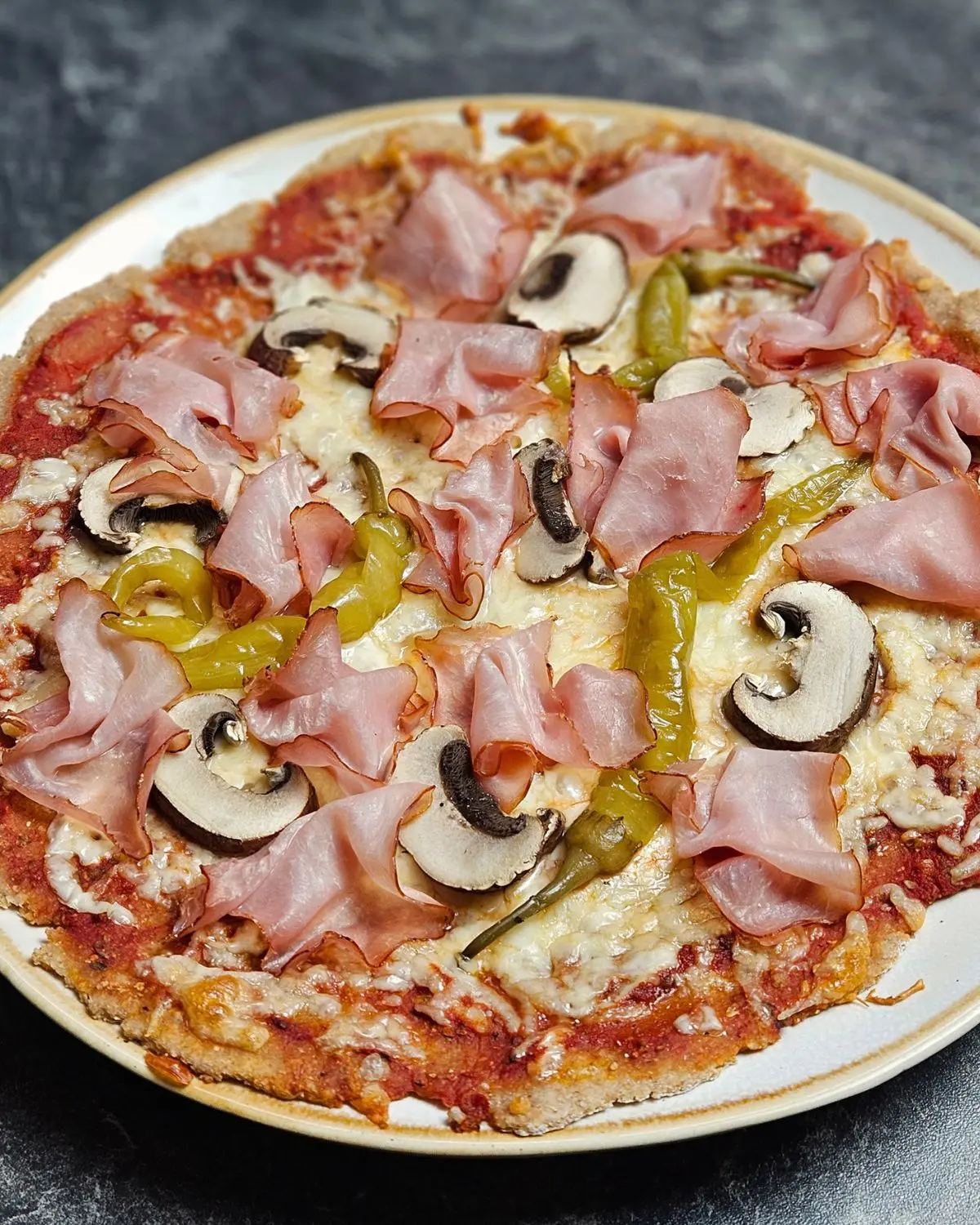 High Protein Pizza mit Skyr-Teig mit Schinken, Champignons und Pepperoni belegt und auf einem Teller serviert