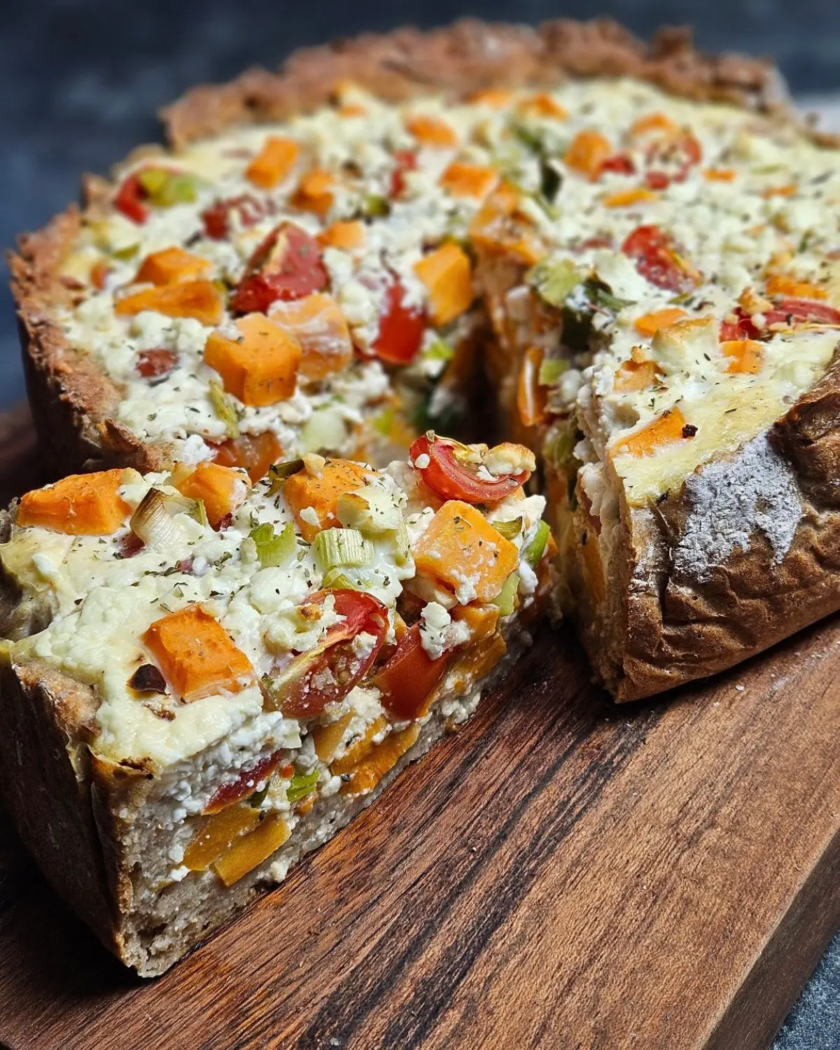 High Protein Süßkartoffel-Quiche mit Lauch und Tomaten auf einem rustikalen Brett angerichtet