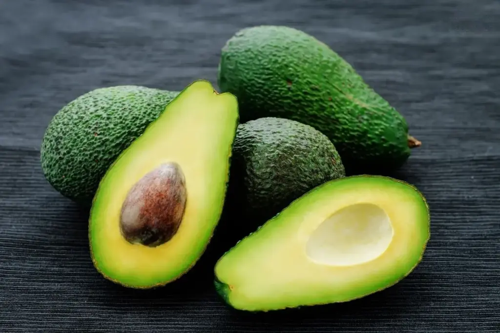 4 Avocados, eine ist in zwei Hälften aufgeschnitten