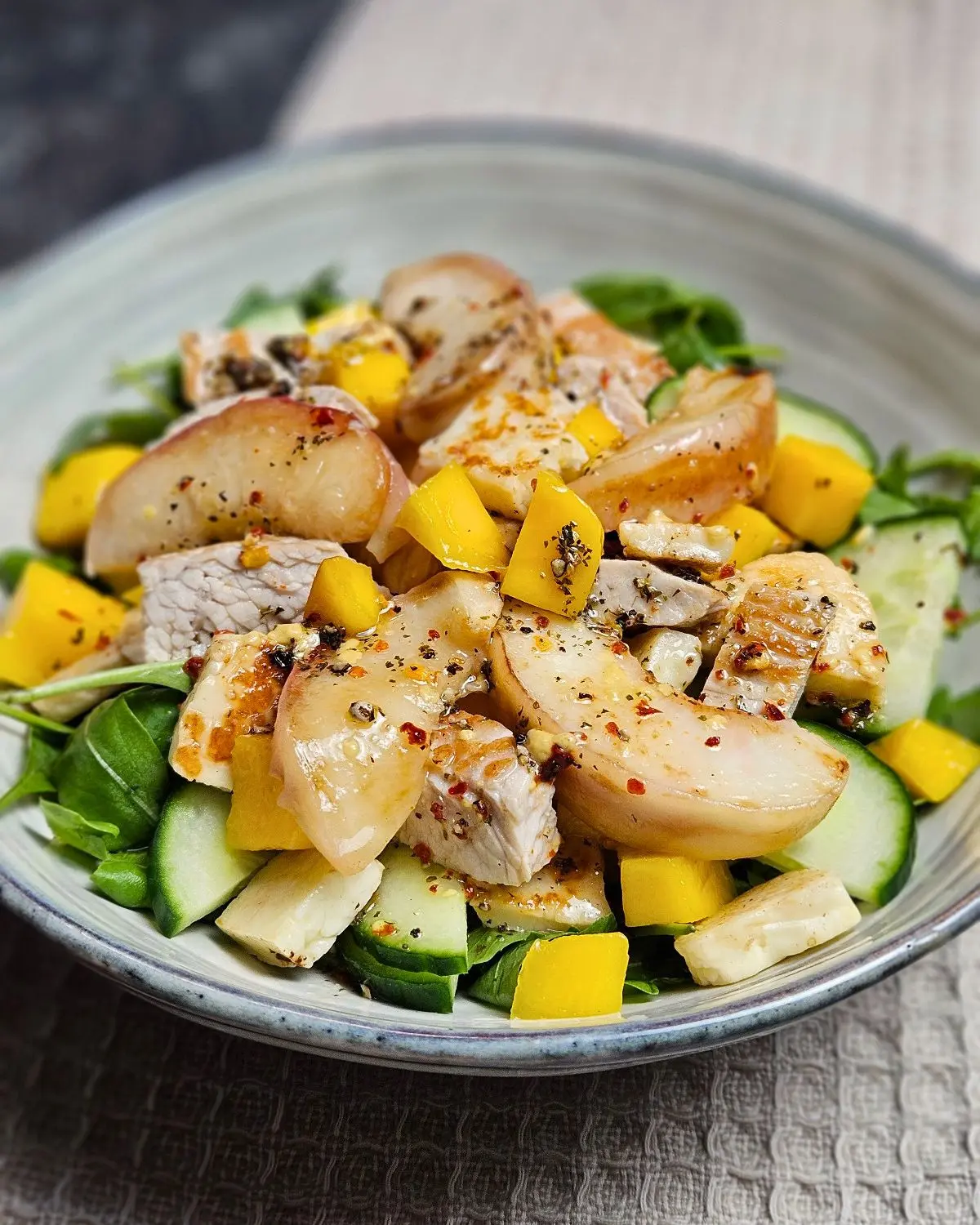 Fruchtiger Aprikose-Mango-Salat mit Putenstreifen und Halloumi in einer Schüssel angerichtet