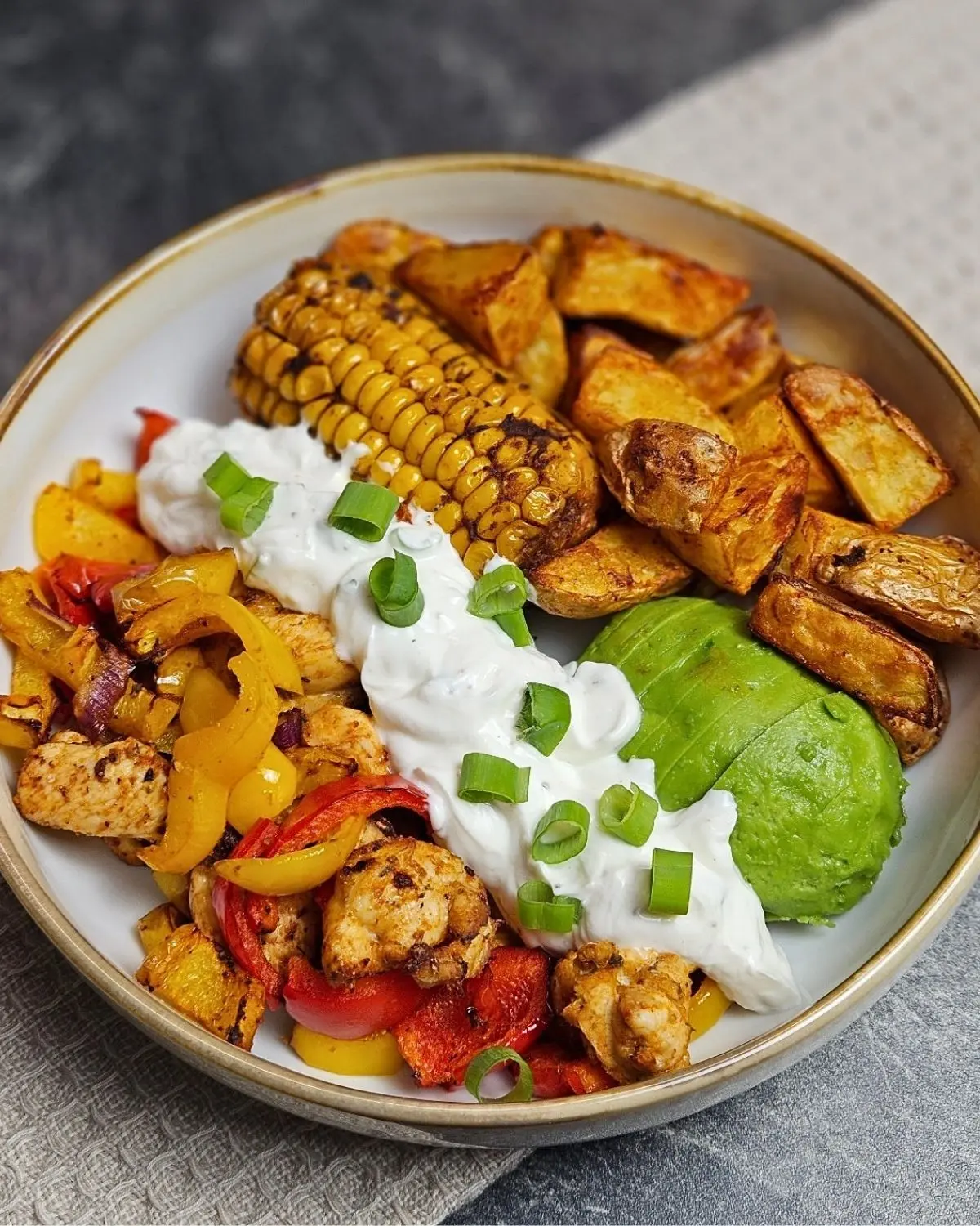 Hähnchen-Fajita Bowl mit Mais, Avocado und Kartoffelecken in einer Bowl angerichtet