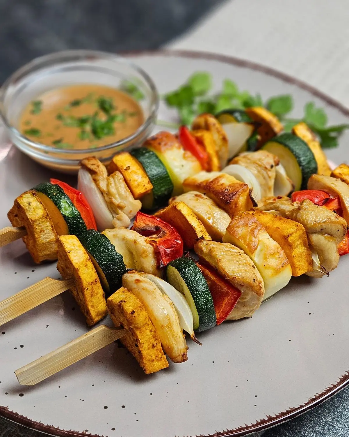 Hähnchen-Halloumi-Spieße mit Erdnusssauce - Airfryer Edition, 3 Spieße mit einer Schale Erdnusssauce auf einem Teller angerichtet