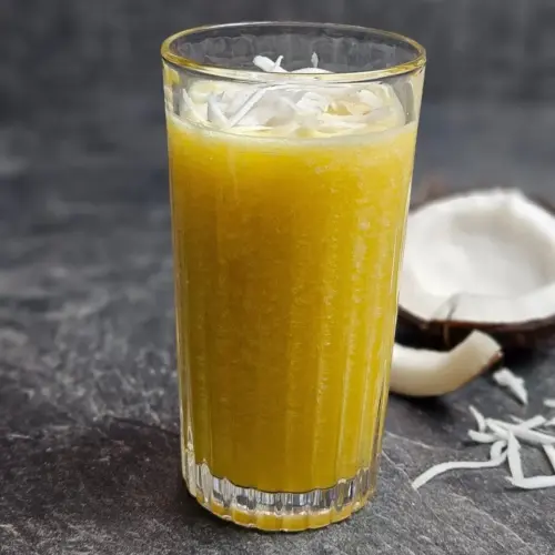 High Protein Kokos-Mango-Shake in einem Glas, mit einer halben Kokosnuss daneben