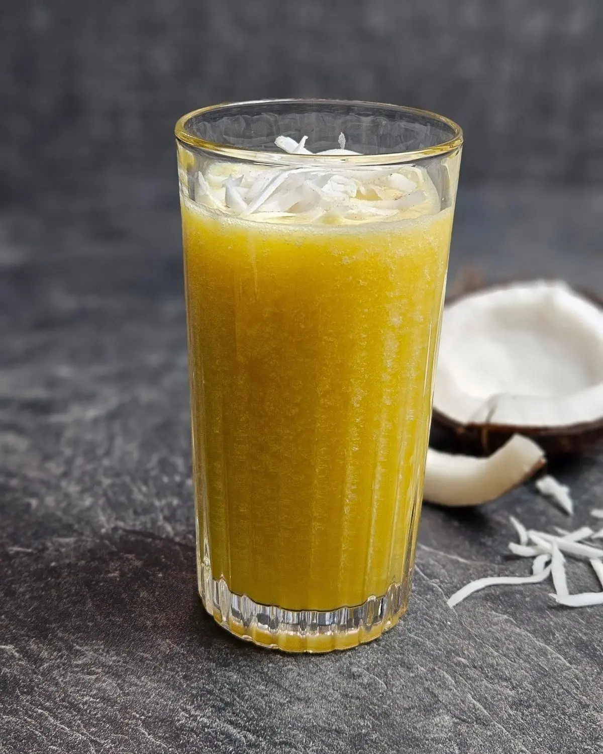 High Protein Kokos-Mango-Shake in einem Glas, mit einer halben Kokosnuss daneben