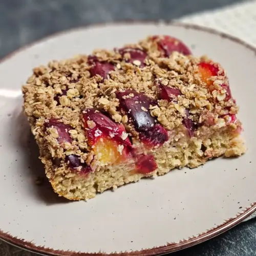 Ein Stück High Protein Zwetschgenkuchen mit Haferflockenstreusel auf einem Teller angerichtet