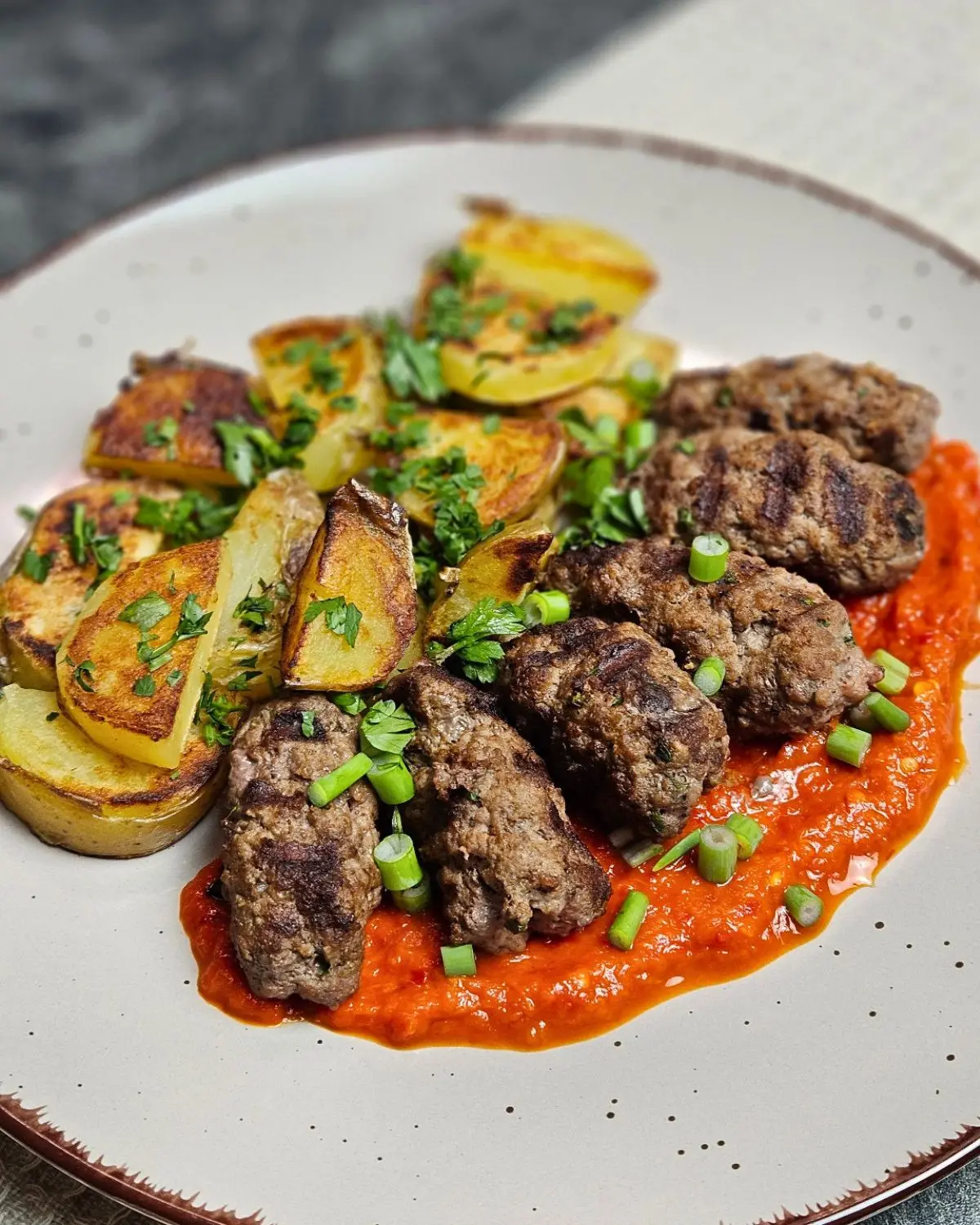 Selbstgemachte Cevapcici mit knusprigen Bratkartoffeln mit Ajvar auf einem Teller serviert