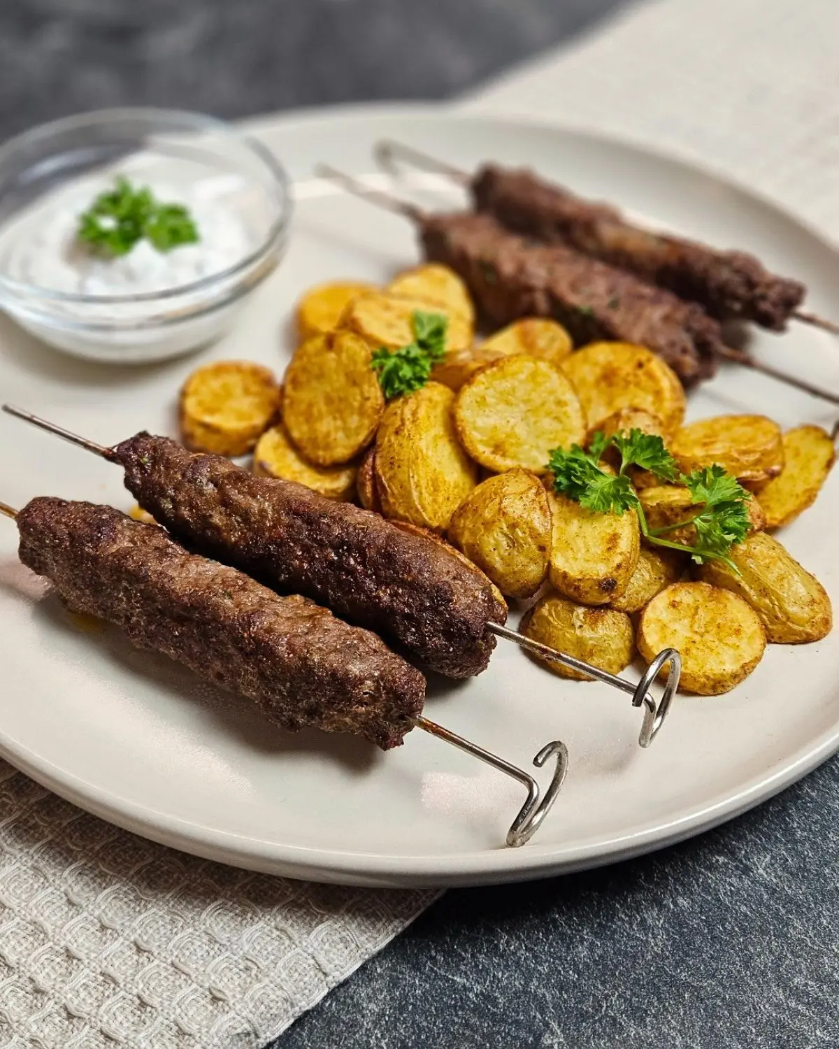 Adana-Kebab-Spieße mit Kartoffeln und selbstgemachtem Dip auf einem Teller angerichtet