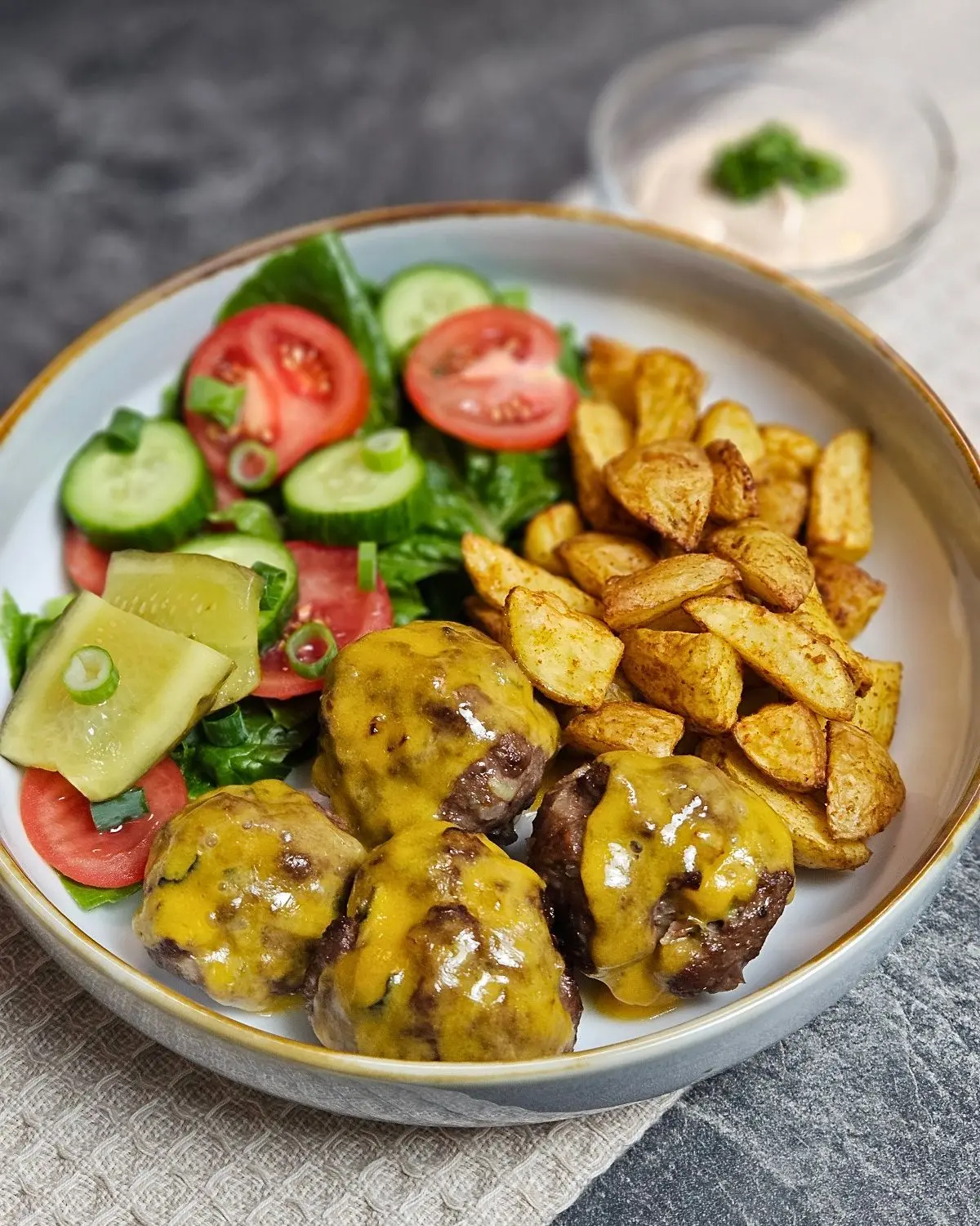 Cheeseburger-Bowl mit Hackbällchen und Kartoffelecken und Salat in einer Bowlschüssel angerichtet