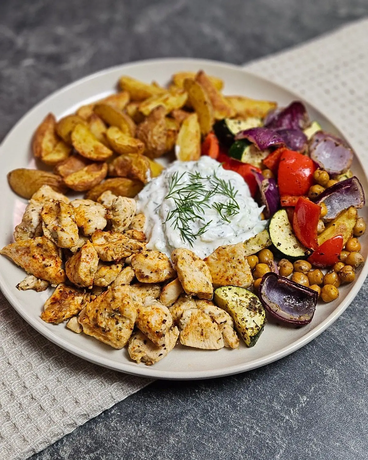 Gyros-Hähnchen mit Ofengemüse und Kartoffelspalten aus dem Airfryer auf einem Teller angerichtet